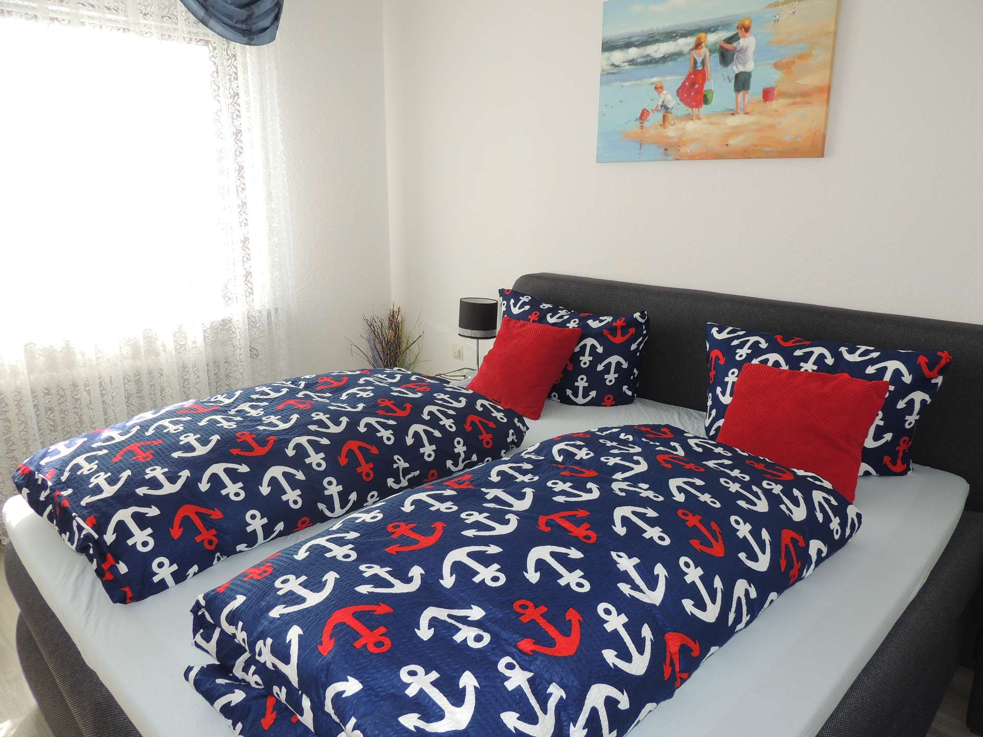 Doppelbett mit blau-weiß-roter Bettwäsche mit Ankermotiven und roten Zierkissen