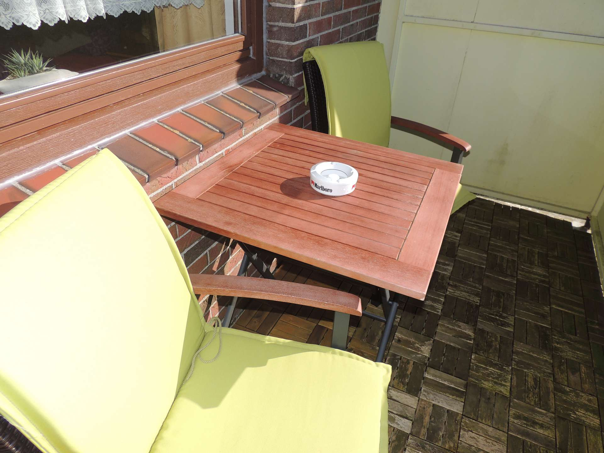 Balkon mit zwei Stühlen mit grünen Auflagen und Holztisch mit Aschenbecher