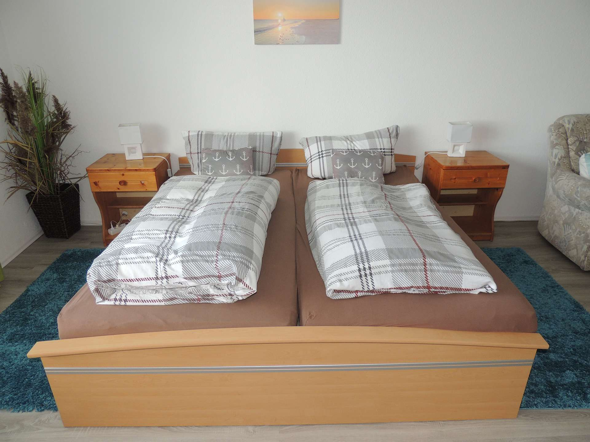 Blick auf Doppelbett aus hellem Holz mit weiß-grauem Bettzeug, dazu Nachttische rechts und links davon